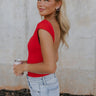 Upper body side view of female model wearing the Ryleigh Red Backless Bodysuit that has red knit fabric, an open back, and a scoop neckline. Worn with jeans.