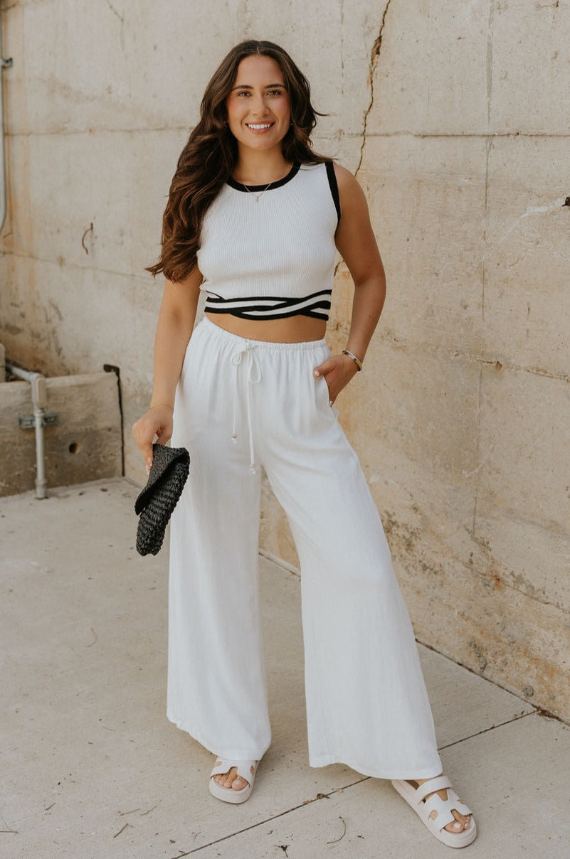 Full body view of female model wearing the Lucia White & Black Groovy Hem Tank which features White Ribbed Fabric, Cropped Tank,  Black Intertwine Hem Detail, Round Neckline and Sleeveless