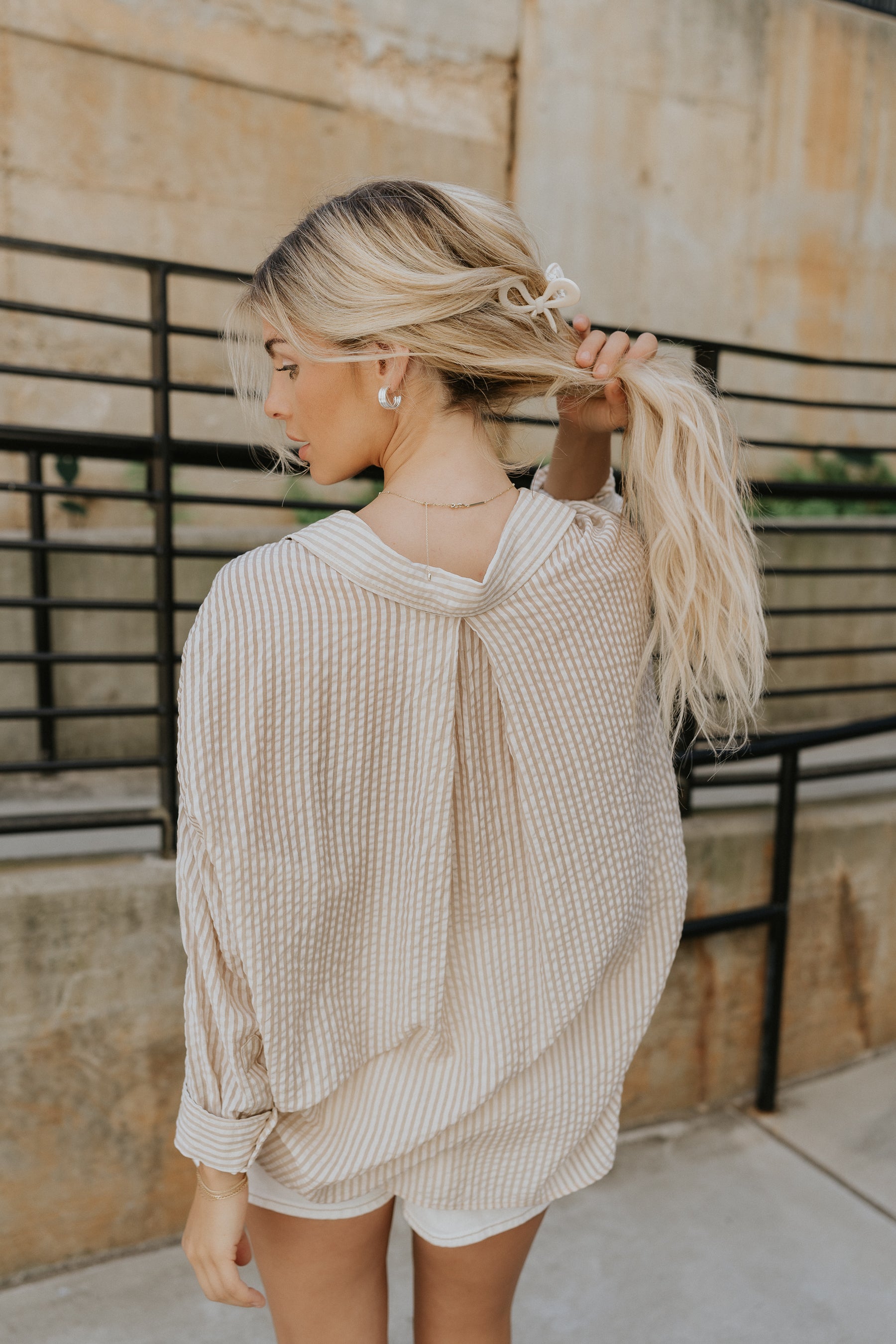 Back view of a female wearing the Madison button up stripe blouse.  It features beige and white vertical stripes.