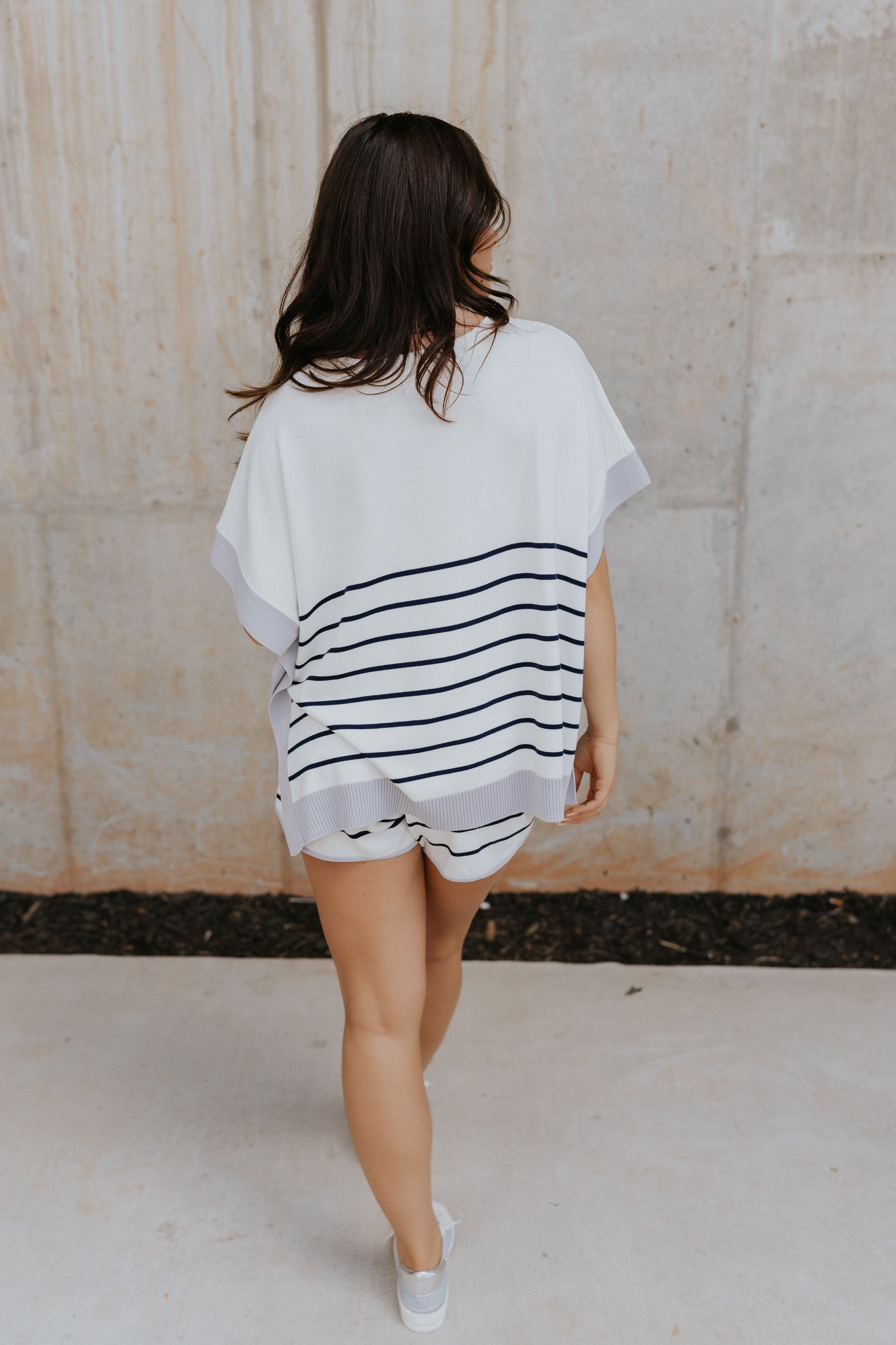 Back view of female model wearing the Bella Rose Stipe Top. This top is short sleeve with navy and ivory stripes and trimmed in lavender with a crew neck.