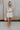 Full body view of female model wearing the Teagan White Square Neckline Romper which features White Linen Fabric, White Lining. Square Neckline, Sleeveless and Monochrome Back Zipper with Hook Closure