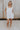 Full body view of female model wearing the Teagan White Square Neckline Romper which features White Linen Fabric, White Lining. Square Neckline, Sleeveless and Monochrome Back Zipper with Hook Closure