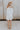 Full body back view of female model wearing the Teagan White Square Neckline Romper which features White Linen Fabric, White Lining. Square Neckline, Sleeveless and Monochrome Back Zipper with Hook Closure
