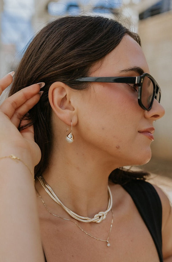 Model is seen from the side moving her hair to reveal the Lily Earrings.