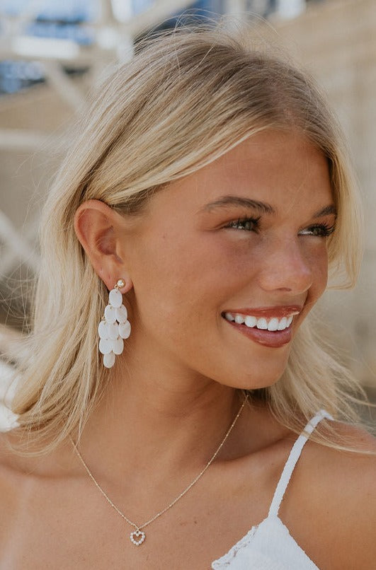 Model is shown turned to the side. She is wearing the Vanessa Dangle Earrings that feature tiered white iridescent beads.