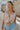 Front view of female model wearing the Emilia Satin Plunge Neckline Sleeveless Bodysuit which features Satin Fabric, Surplice Neckline with Button Snap, Sleeveless and Thong Bottom with Button Closure. the bodysuit is available in taupe and white