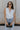 Front view of female model wearing the Emilia Satin Plunge Neckline Sleeveless Bodysuit which features Satin Fabric, Surplice Neckline with Button Snap, Sleeveless and Thong Bottom with Button Closure. the bodysuit is available in taupe and white