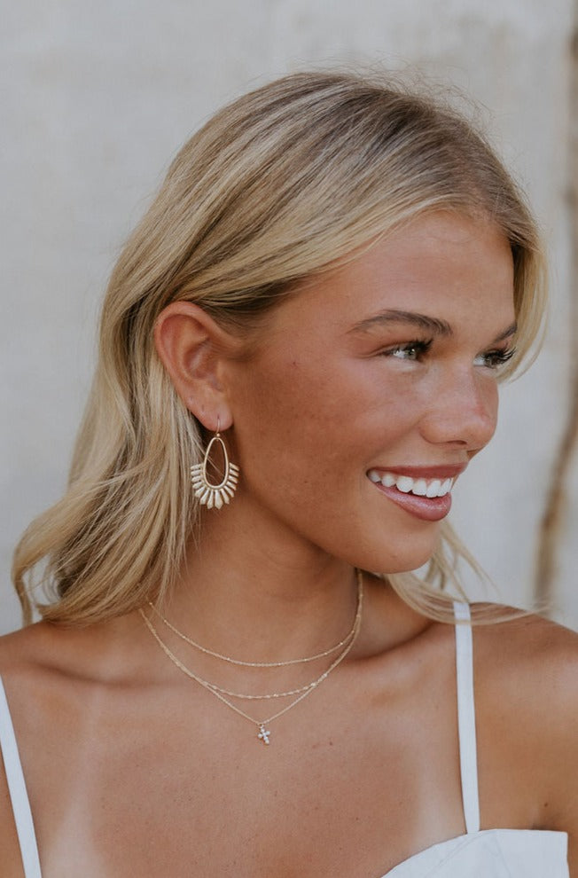 Model is shown wearing the Jordyn earrings that have teardrop dangles with radiating geometric lines.
