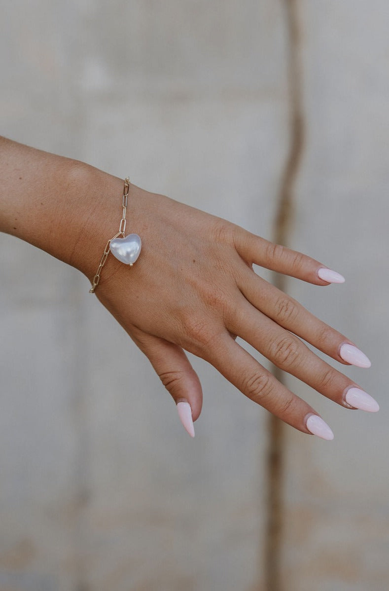 The hand of a model is shown with the Gia Heart Bracelet clasped on her wrist.