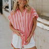 front view of female model wearing the Sienna Pink & Red Stripe Button-Up Short Sleeve Top which features Red and Pink Stripe Pattern, Scooped Hem, Slit Details on each side, Wooden Front Button-Up, Collared Neckline and Short Sleeves