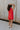 Full body back view of female model wearing the Athena Front Zip-Up Halter Romper which features Denim Like Fabric, Pockets on each side, Two Back Pockets, Folded Hem Details, Front Zipper Closure, Collared Neckline and Sleeveless. the romper is available in red and black