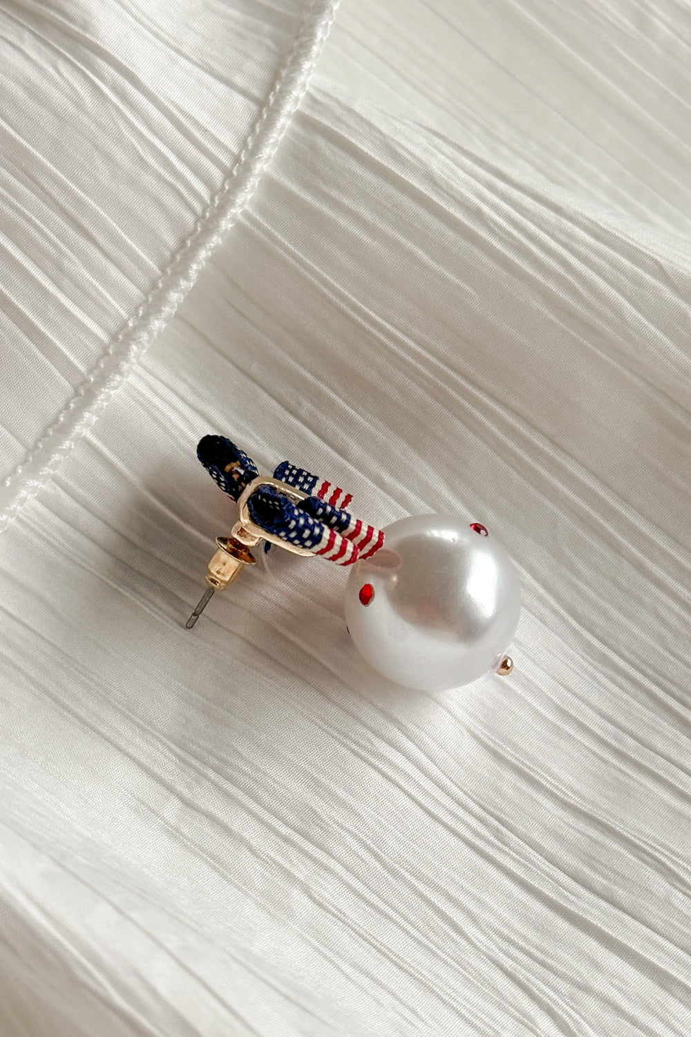 Close-up side view image of the Betsy Red, White, & Blue Pearl Earring against a white background. Earrings have american flag bows and a pearl pendant with red white and blue stones.