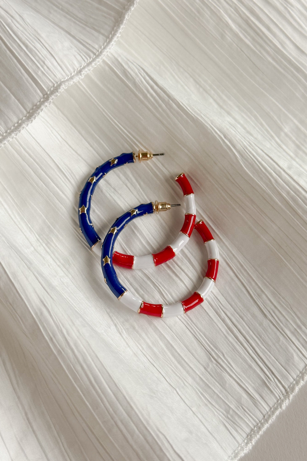 Image shows Eleanor Red, White, & Blue Hoop Earrings on top of each other against a white background. Earrings feature red and white striped and a blue section with gold stars.