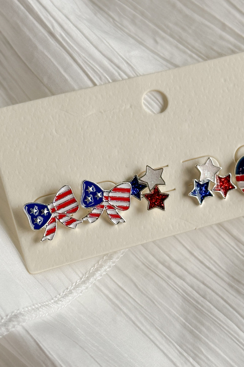Image shows close-up of bows in Kennedy Stars & Stripes Stud Set that have 3 pairs or studs; bows, circles, and stars. Studs are red white and blue with stripe details.