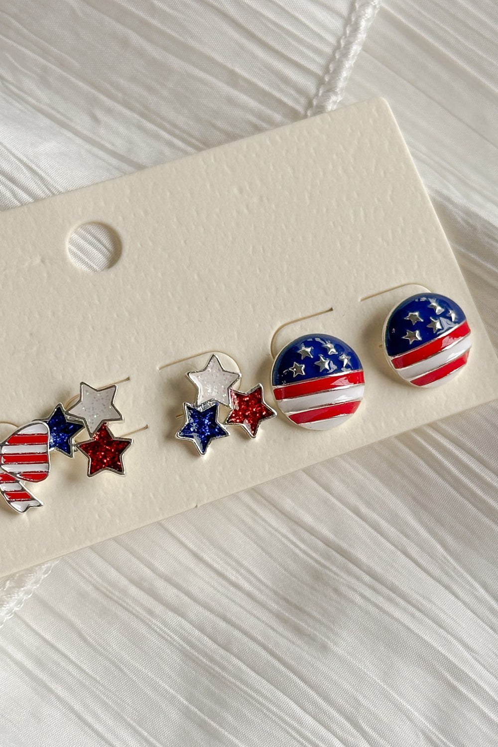 Image shows close-up of circles Kennedy Stars & Stripes Stud Set that have 3 pairs or studs; bows, circles, and stars. Studs are red white and blue with stripe details.
