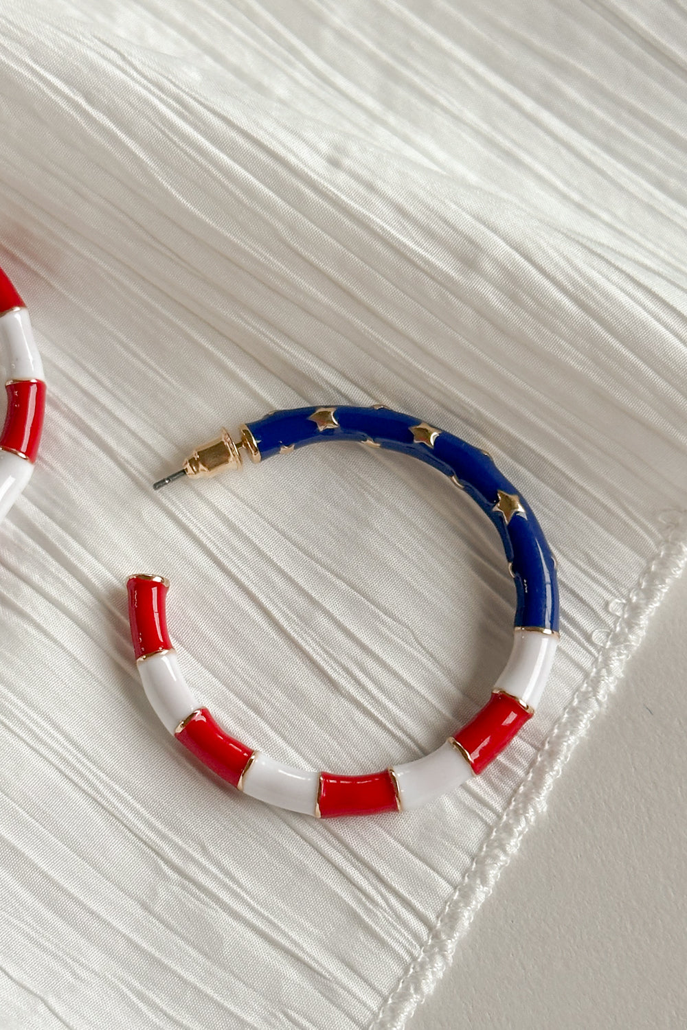 Image shows close-up of Eleanor Red, White, & Blue Hoop Earrings against a white background. Earrings feature red and white striped and a blue section with gold stars.