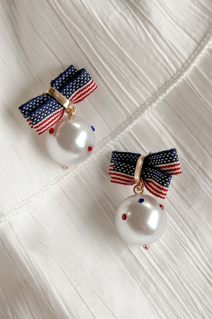 Image of the Betsy Red, White, & Blue Pearl Earrings against a white background. Earrings have american flag bows and a pearl pendant with red white and blue stones.