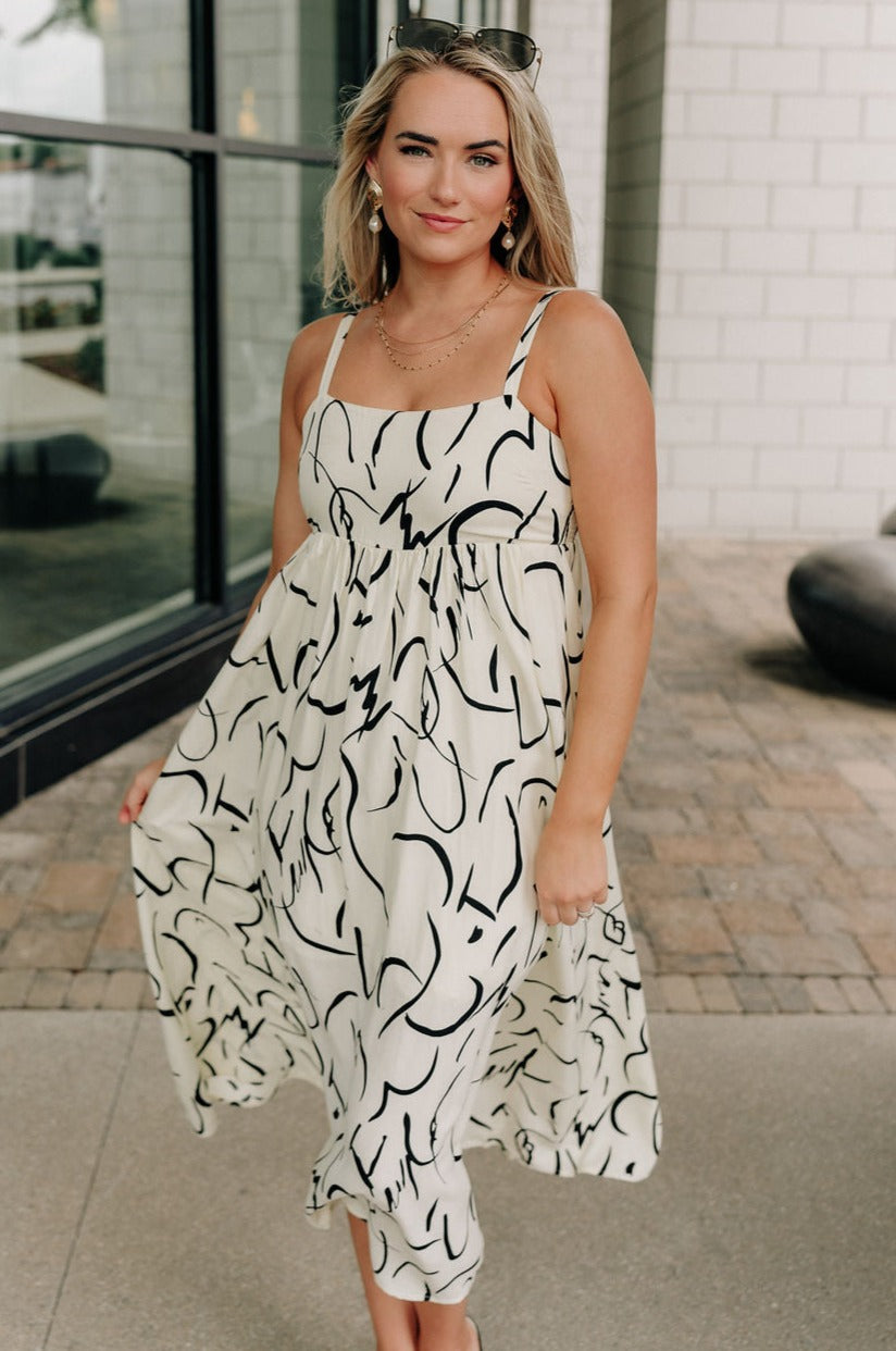 Full body view of female model wearing the Luna Ivory & Black Abstract Midi Dress which features Cream and Black Lightweight Fabric, Abstract Print, Midi Length, Cream Lining, Square Neckline, Adjustable Straps and Smocked Back