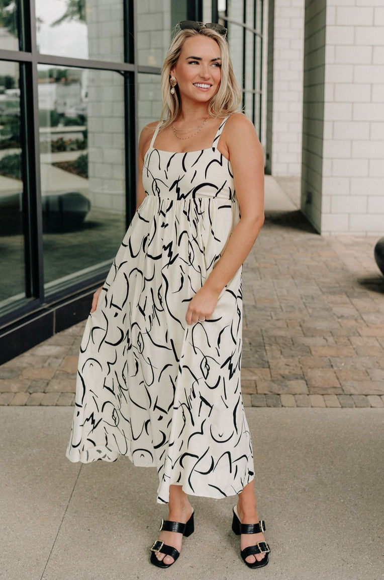 Full body view of female model wearing the Luna Ivory & Black Abstract Midi Dress which features Cream and Black Lightweight Fabric, Abstract Print, Midi Length,  Cream Lining, Square Neckline, Adjustable Straps and Smocked Back