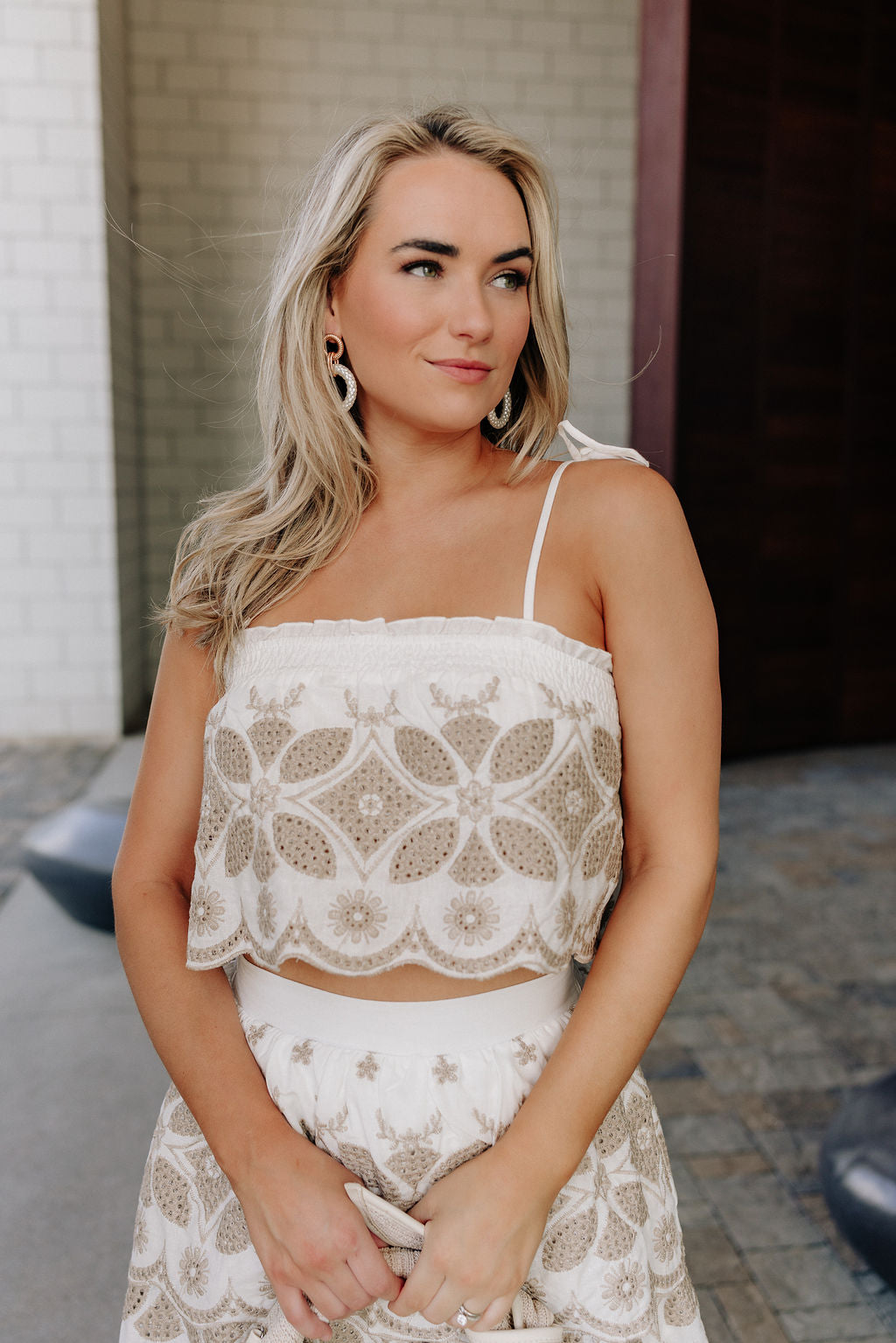 close up view of female model wearing the Alexandra White & Taupe Eyelet Tank which features White and Taupe Fabric, Eyelet Pattern, Scallop Hem, Ruffle Details, Square Neckline, White Lining and Tie Straps