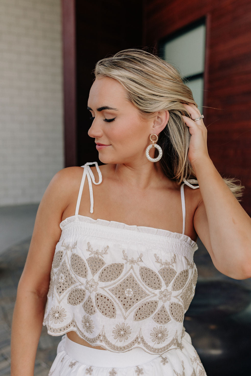 close up view of female model wearing the Alexandra White & Taupe Eyelet Tank which features White and Taupe Fabric, Eyelet Pattern, Scallop Hem, Ruffle Details, Square Neckline, White Lining and Tie Straps