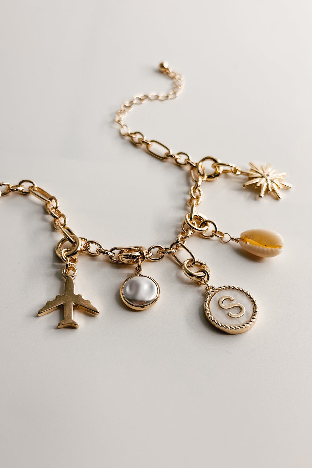 Image shows a gold chain link bracelet with assorted charms. 'S' alphabet charm is shown in the center.