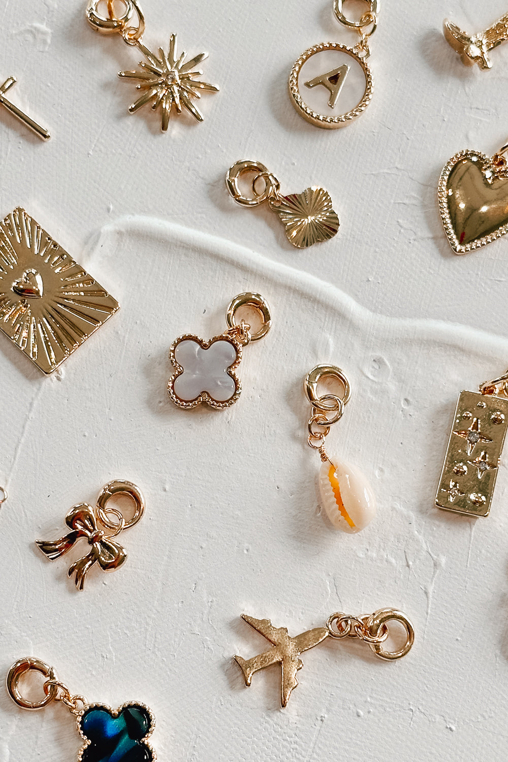 Image shows assorted charms against a white background. Charms pictured include white clover, gold clover, heart, star medallion, airplane, black clover, bow, cowboy boy, heart medallion, and starbust.