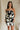 front view of female model wearing the Lila Black & Cream Tie Straps Romper which features Black and White Geometric Pattern, White Shorts Lining, Two Side Pockets, Ruffle Upper, Square Neckline and Tie Straps