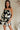 front view of female model wearing the Lila Black & Cream Tie Straps Romper which features Black and White Geometric Pattern, White Shorts Lining, Two Side Pockets, Ruffle Upper, Square Neckline and Tie Straps