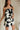 side view of female model wearing the Lila Black & Cream Tie Straps Romper which features Black and White Geometric Pattern, White Shorts Lining, Two Side Pockets, Ruffle Upper, Square Neckline and Tie Straps