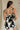 back view of female model wearing the Lila Black & Cream Tie Straps Romper which features Black and White Geometric Pattern, White Shorts Lining, Two Side Pockets, Ruffle Upper, Square Neckline and Tie Straps