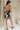 full body back view of female model wearing the Lila Black & Cream Tie Straps Romper which features Black and White Geometric Pattern, White Shorts Lining, Two Side Pockets, Ruffle Upper, Square Neckline and Tie Straps
