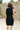 Close up back view of model wearing the Laila Mini Sweater Dress in black. This is a sweater mini dress, sleeveless, comes in either black or chestnut.