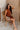 Full body view of female model sitting while wearing the Monica Rust Mock Neck Sweater Dress that has rust colored knit fabric, a mock neck, and mini length hem.