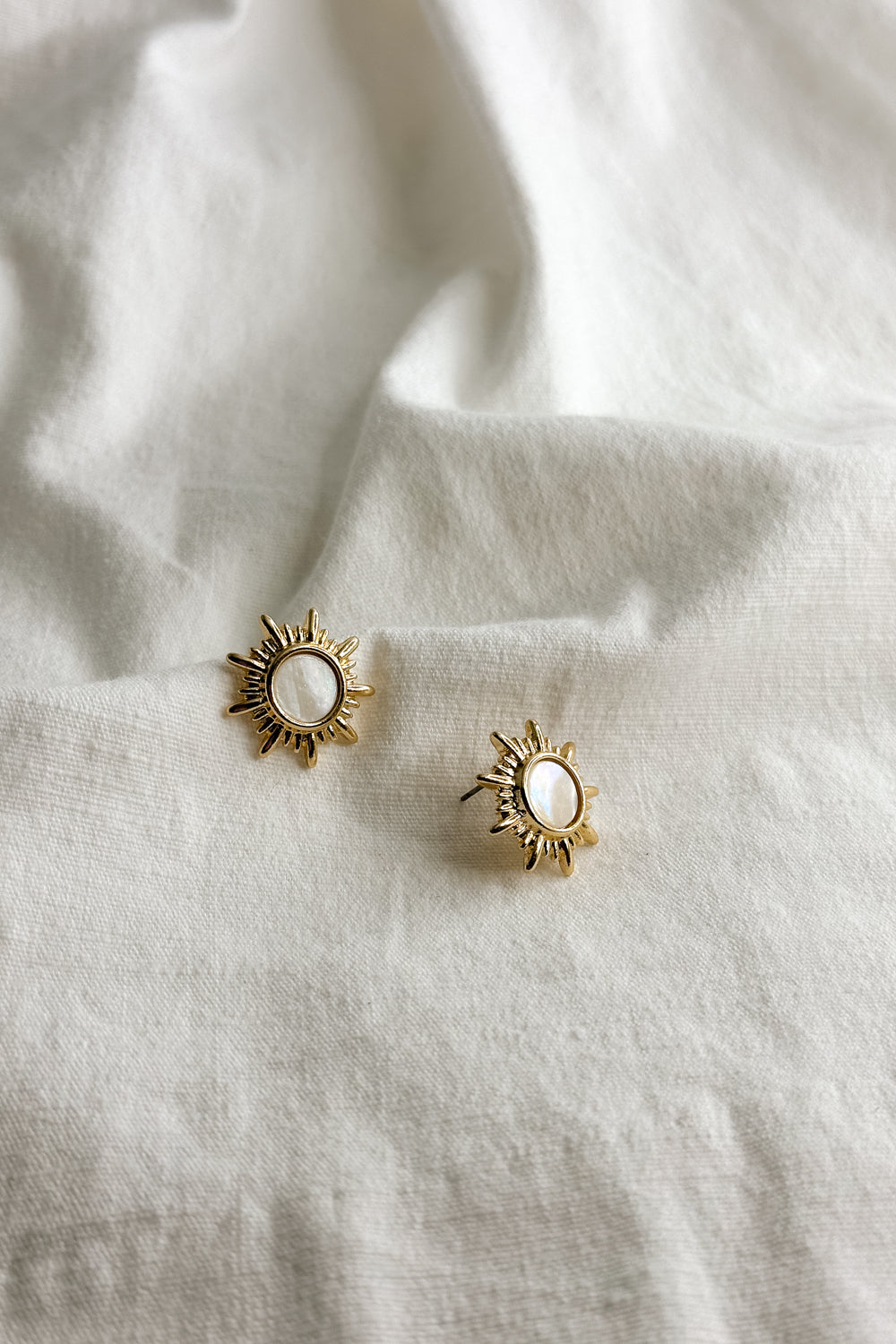 Flat lay view of Faith Gold & White Starburst Stud Earring which features old starburst studs with white stone