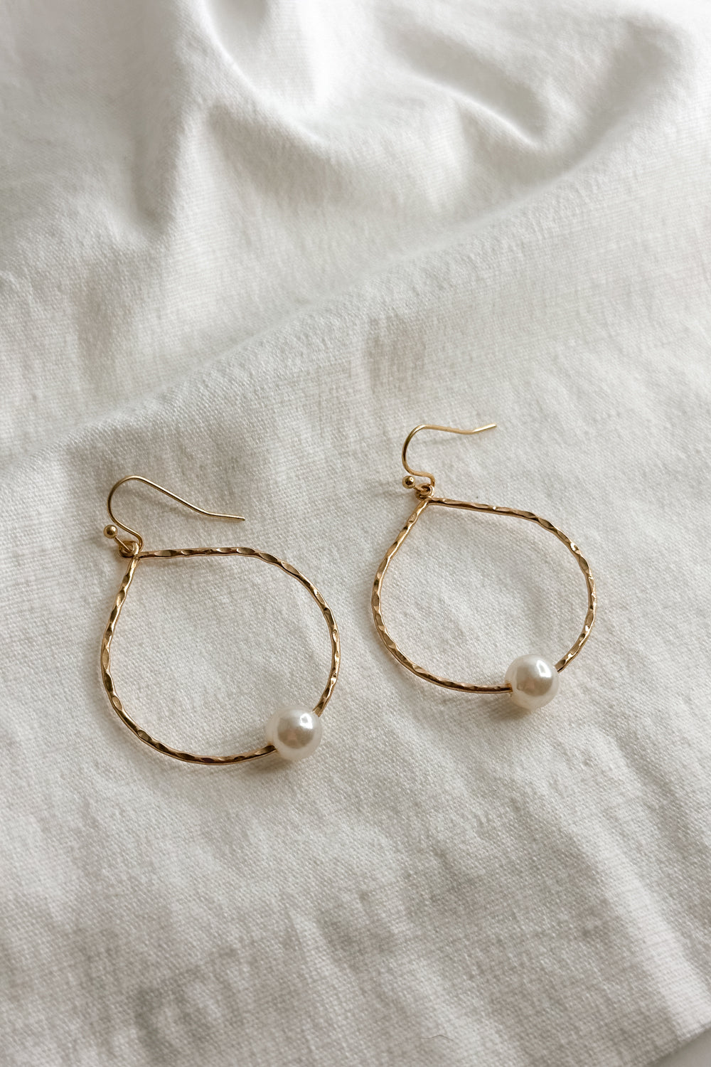 Flat lay view of the Elizabeth Gold Pearl Hoop Dangle Earring which features open hammered, gold hoop with single pearl detail