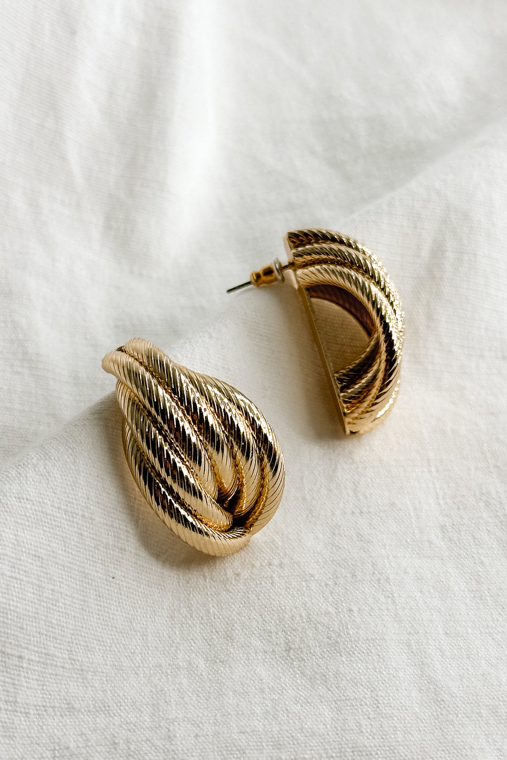 Flat lay view of the Stella Gold Rope Dangle Stud Earring which features oversized, gold rope studs