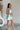 Full body side view of female model wearing the Dorit Light Blue Satin Mini Dress which features Light Blue Shimmer Fabric, Mini Length, Cowl Neckline and Skinny Straps