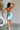 Full body back view of female model wearing the Dorit Light Blue Satin Mini Dress which features Light Blue Shimmer Fabric, Mini Length, Cowl Neckline and Skinny Straps