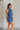 Side view of female model wearing the Leila Dark Blue Halter Neckline Romper which features Grey Blue Textured Fabric, Two Side Slit Pockets, Halter Neckline with Tie, Elastic Waistband and Back Key Hole