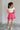 Full body back view of female model wearing the Gabriella Pink Ruffle Mini Skort which features Pink Lightweight Fabric, Pink Shorts Lining, Ruffle Pleated Hem Details and Side Tie Detail