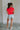 Full body back view of female model wearing the Evie Red Coral Short Sleeve Top which features Coral Red Cotton Fabric, Cropped Waist with Raw Hem, Round Neckline and Short Sleeves