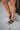 Right side view of female model wearing the Clemons Sandal in Black which features Black Faux Leather, Upper Strappy Details and Corked Covered Padded Footbed