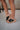 Right side view of female model wearing the B.O.C. Born Concept Sunny Wedge Sandal in Black which features Black Faux Leather Upper, Slip-On Style and Criss-Cross Strap & Toe Wrap Detail