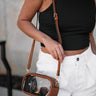 SIde view of female model wearing the Alexandria Clear Purse which features clear with brown leather details, double gold zipper closure, and an adjustable brown leather strap with gold details. 