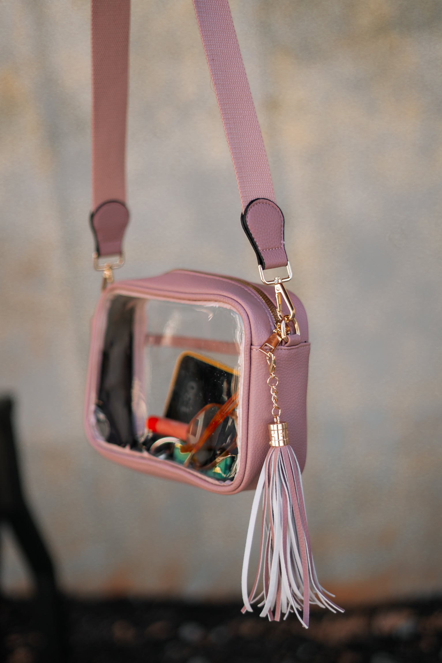 Image shows up close image of the Tiffany Clear Purse in Pink that has a clear rectangle body, pink exterior, a pink strap, and a pink fringe tassel.