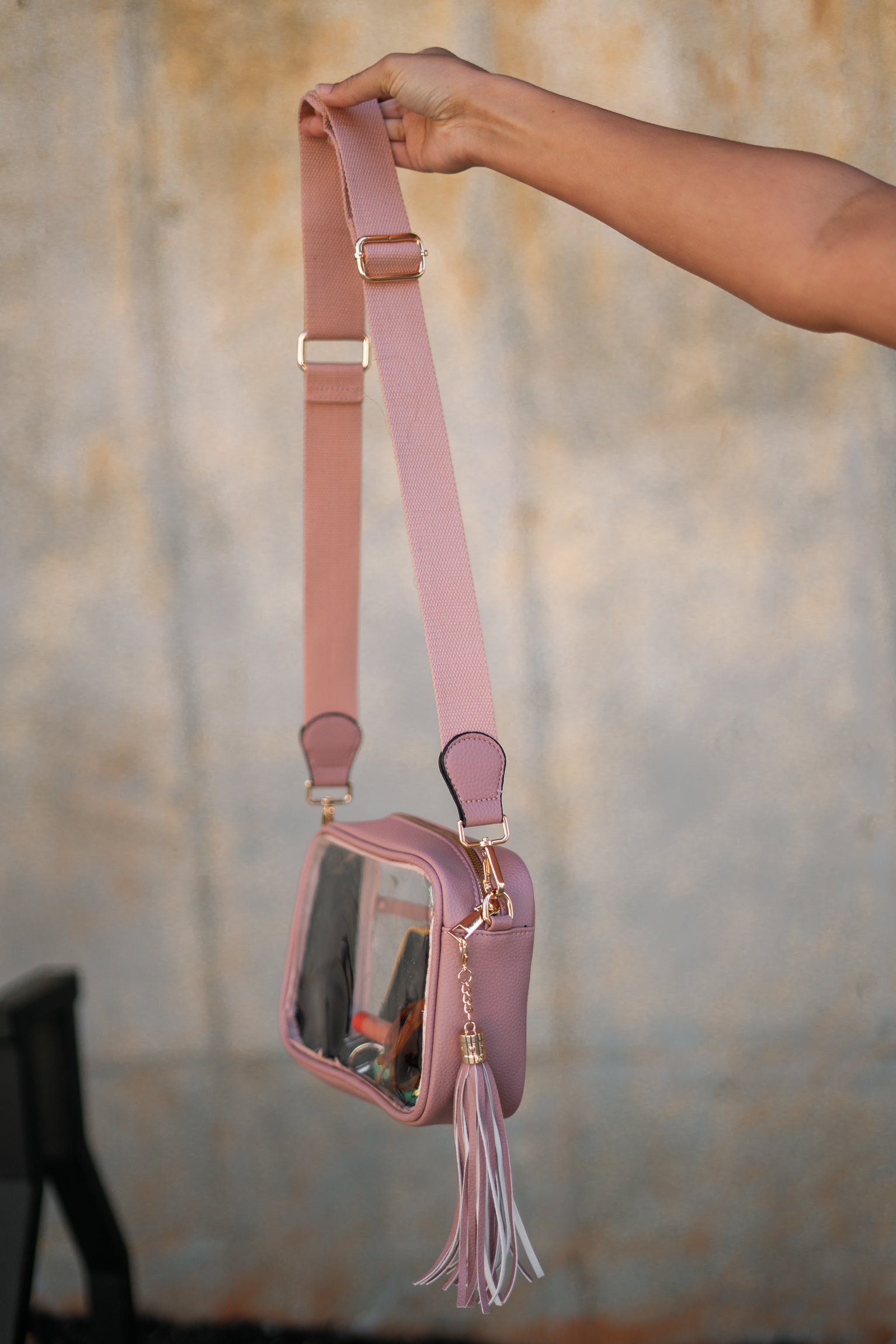 Image shows arm holding the Tiffany Clear Purse in Pink that has a clear rectangle body, pink exterior, a pink strap, and a pink fringe tassel.