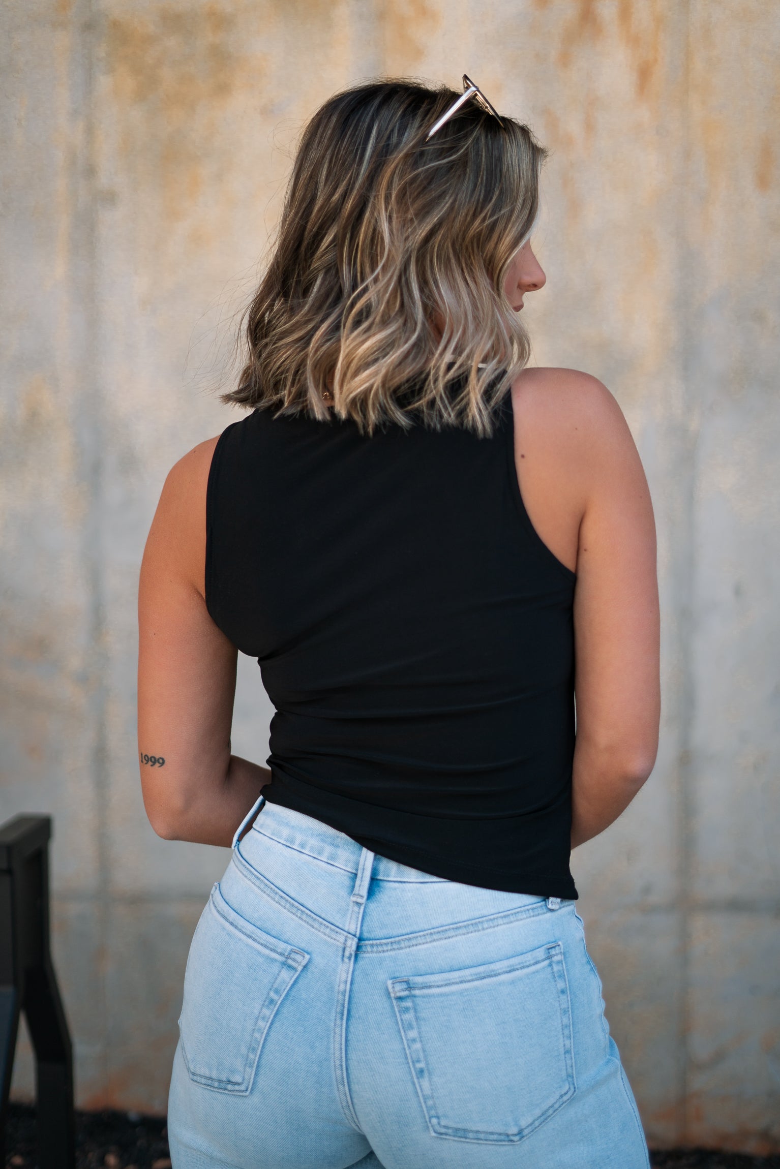 Back view of female model wearing the Brielle Black Sleeveless Tank which features Black Lightweight Fabric, Round Neckline and Sleeveless