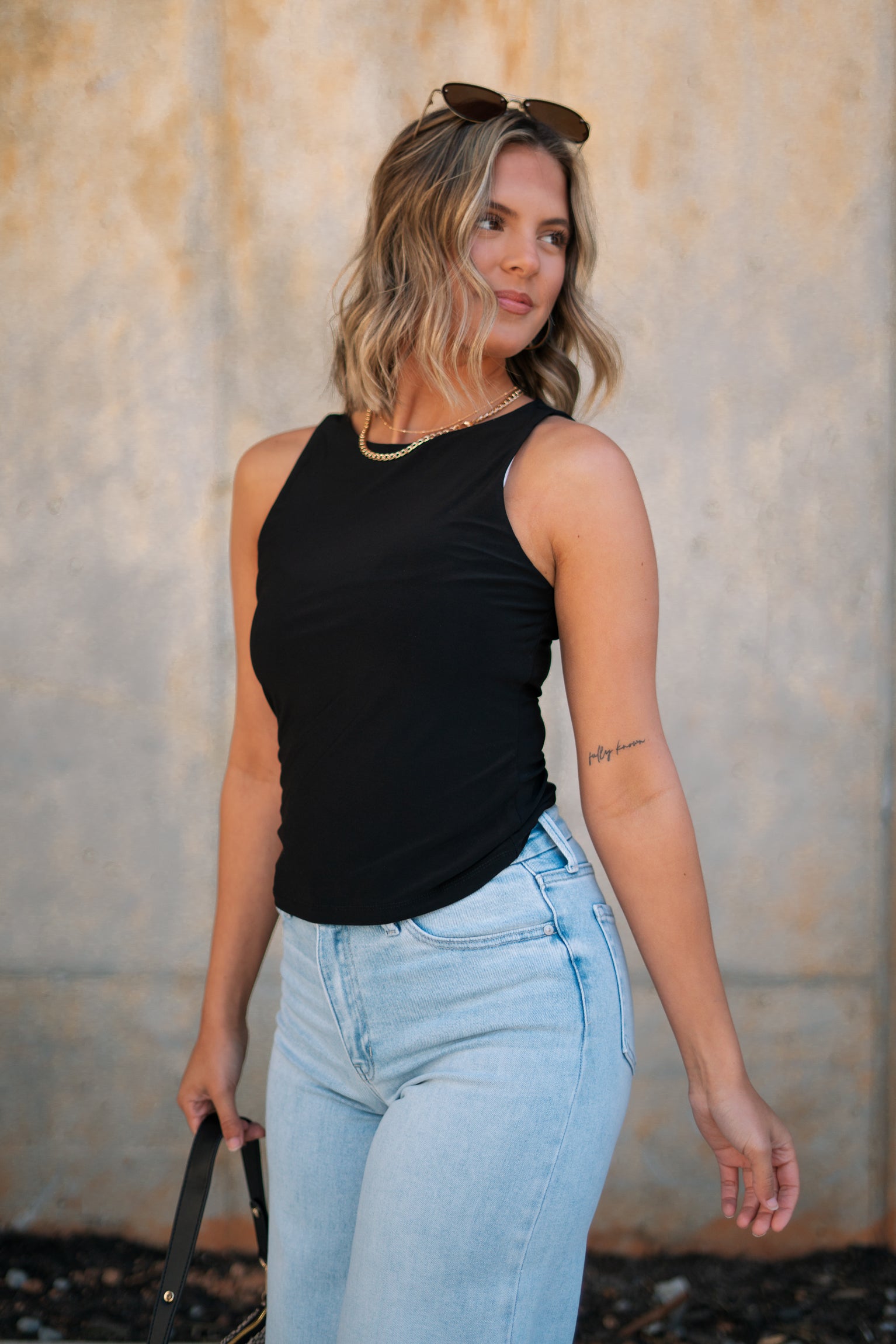 Frontal side view of female model wearing the Brielle Black Sleeveless Tank which features Black Lightweight Fabric, Round Neckline and Sleeveless
