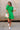 Full body front view of female model wearing the Lea Green Puff Sleeve Mini Dress that has kelly green fabric, a smocked upper with high neck, short puff sleeves, and mini length. Model is holding coffee and has purse on shoulder.